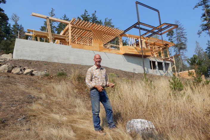 A photograph of Owen Poppy in front of the lighthouse home in progress as built by surfside construction inc.