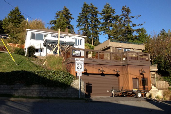 A photo of the new garage built on the lot of the west beach home in white rock bc A photo of a crew member guiding in a beam being craned into the lighthouse home in the sooke bc A photo of one of the large, heavy beams being raised into the lighthouse home in sooke bc as built by surfside construction inc.