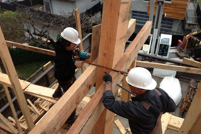 a photo of two carpenters working on one of the beams uses in the west beach home as built by surfside construction inc.