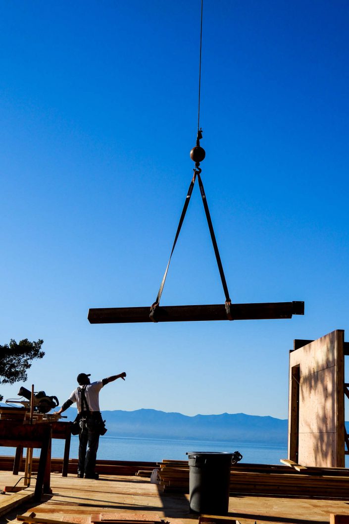 A photo of a crew member guiding in a beam being craned into the lighthouse home in the sooke bc A photo of one of the large, heavy beams being raised into the lighthouse home in sooke bc as built by surfside construction inc.