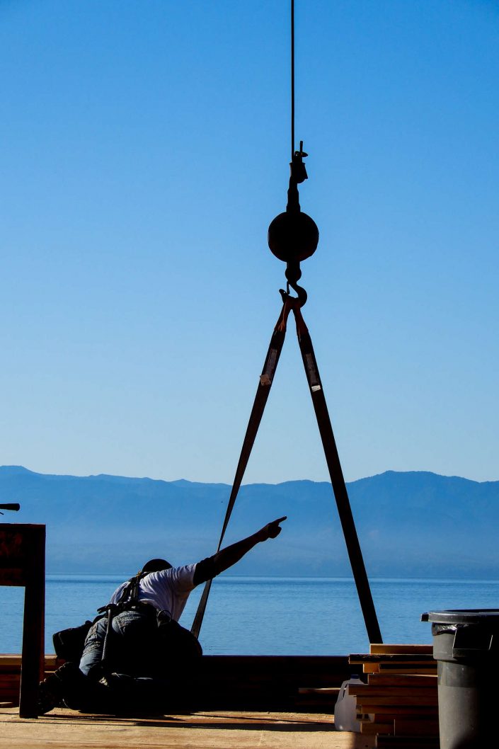 A photo of a crew member setting down a beam being craned into the lighthouse home in the sooke bc A photo of one of the large, heavy beams being raised into the lighthouse home in sooke bc as built by surfside construction inc.