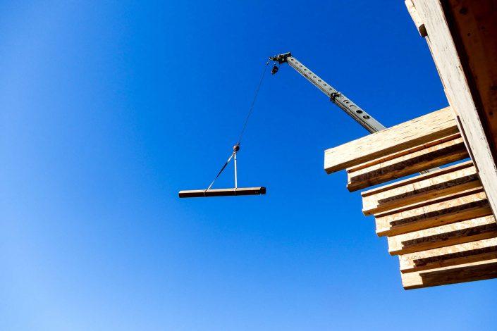 A shot of one of the large beams being craned into the lighthouse home in the sooke bc A photo of a crew member guiding in a beam being craned into the lighthouse home in the sooke bc A photo of one of the large, heavy beams being raised into the lighthouse home in sooke bc as built by surfside construction inc.