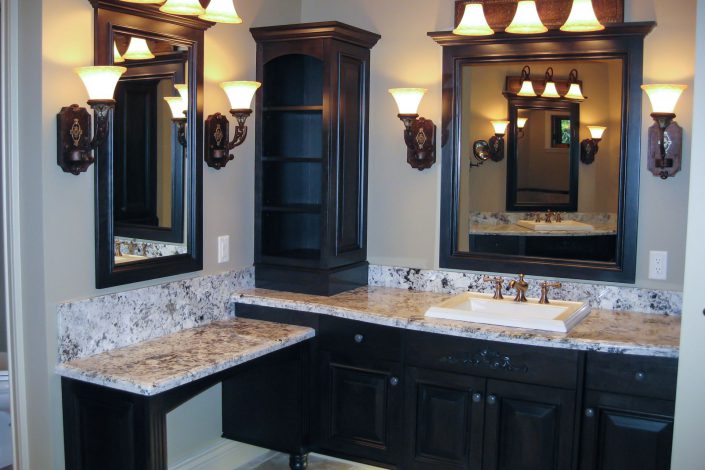 A photo of the ensuite bathroom of the crescent bluff home showing the mirrors, dark wood cabinets and marble counter tops as built by surfside construction inc.